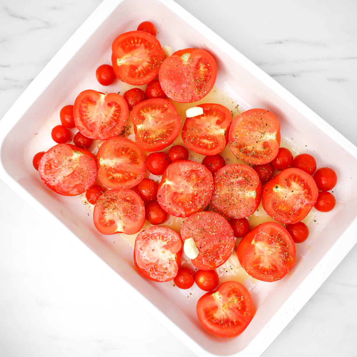 Soupe à la tomate Tomates fraîches coupées et tomates cerises disposées dans un plat allant au four, prêtes à être rôties.