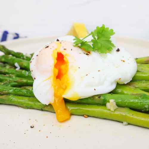 Poached egg with a runny yolk served on roasted asparagus, garnished with a sprig of cilantro.