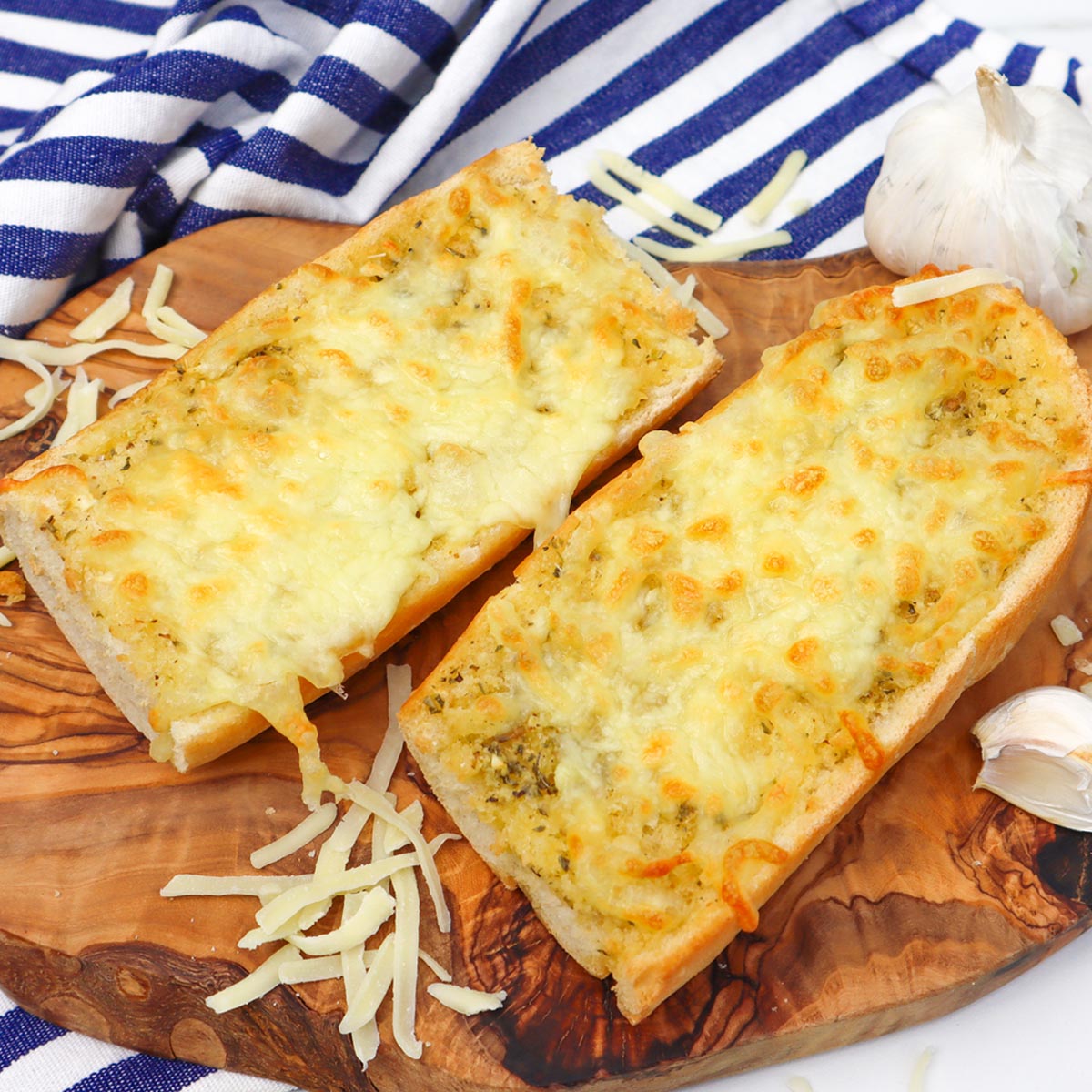 Air Fryer Cheesy Garlic Bread Two pieces of cheesy garlic bread on a wooden board, garnished with garlic and shredded cheese.