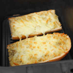 Two pieces of cheesy garlic bread in an air fryer, melted cheese bubbling on top.
