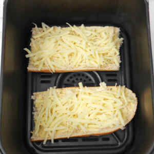 Two pieces of bread topped with shredded cheese in an air fryer basket.