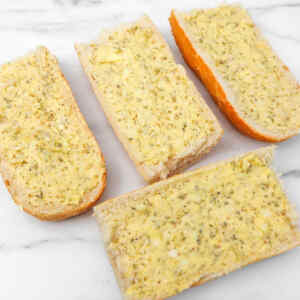 Sliced bread spread with a cheesy garlic mixture, ready for the air fryer.