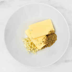 Butter, minced garlic, and herbs in a white bowl, ready for garlic bread preparation.