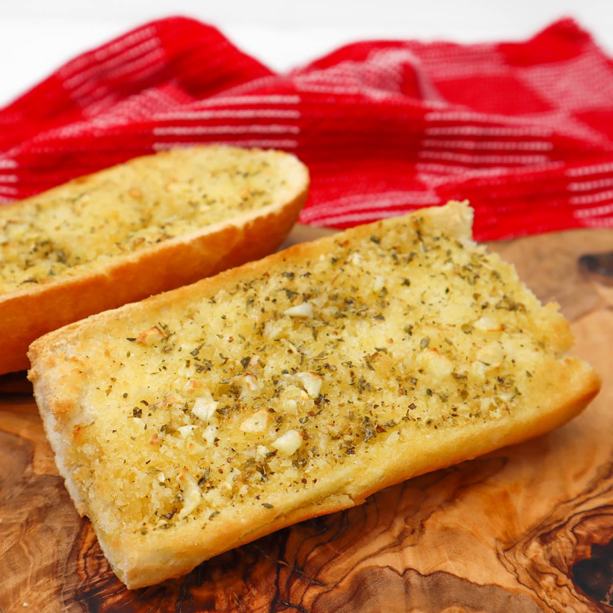 Knoblauchbrot aus der Heißluftfritteuse Zwei Stücke goldbraunes Knoblauchbrot, mit Kräutern bestreut, auf einem Holzschneidebrett.