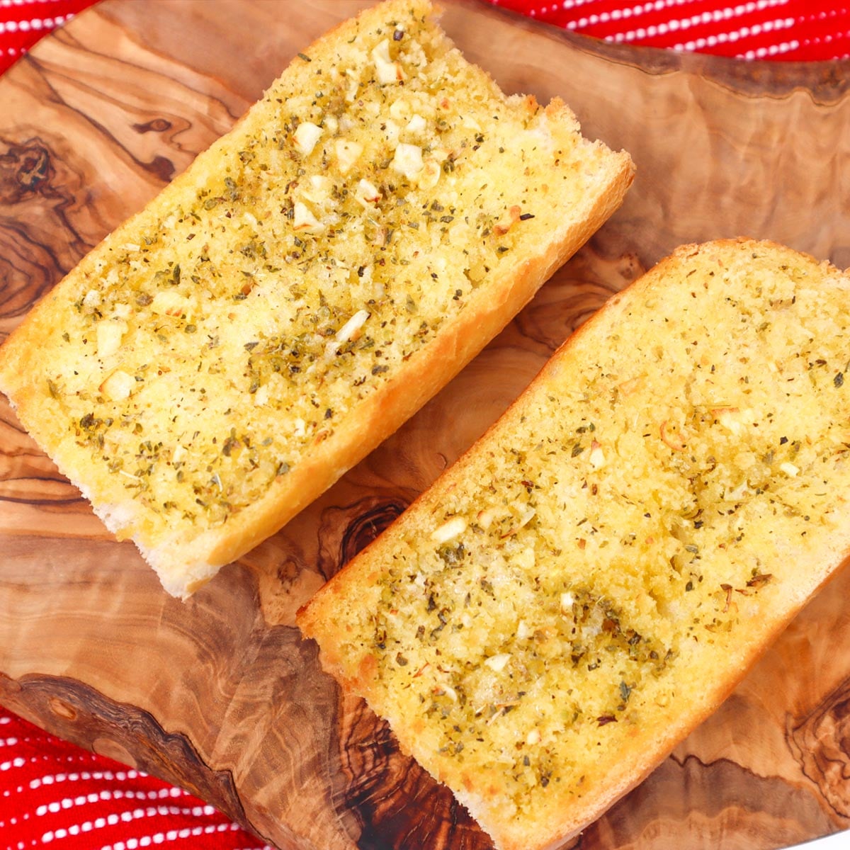 Knoblauchbrot aus der Heißluftfritteuse Zwei Scheiben goldbraunes Knoblauchbrot, mit Kräutern bestreut, auf einem Holzbrett.