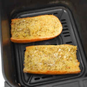 Zwei Scheiben Knoblauchbrot im Airfryer-Korb, goldbraun und mit Kräutern bestreut.