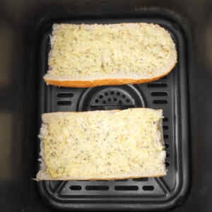 Zwei mit Knoblauchbutter bestrichene Brotscheiben in den Korb einer Heißluftfritteuse geben.