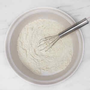 Un bol de farine avec un fouet à l'intérieur, prêt pour la préparation des crêpes.