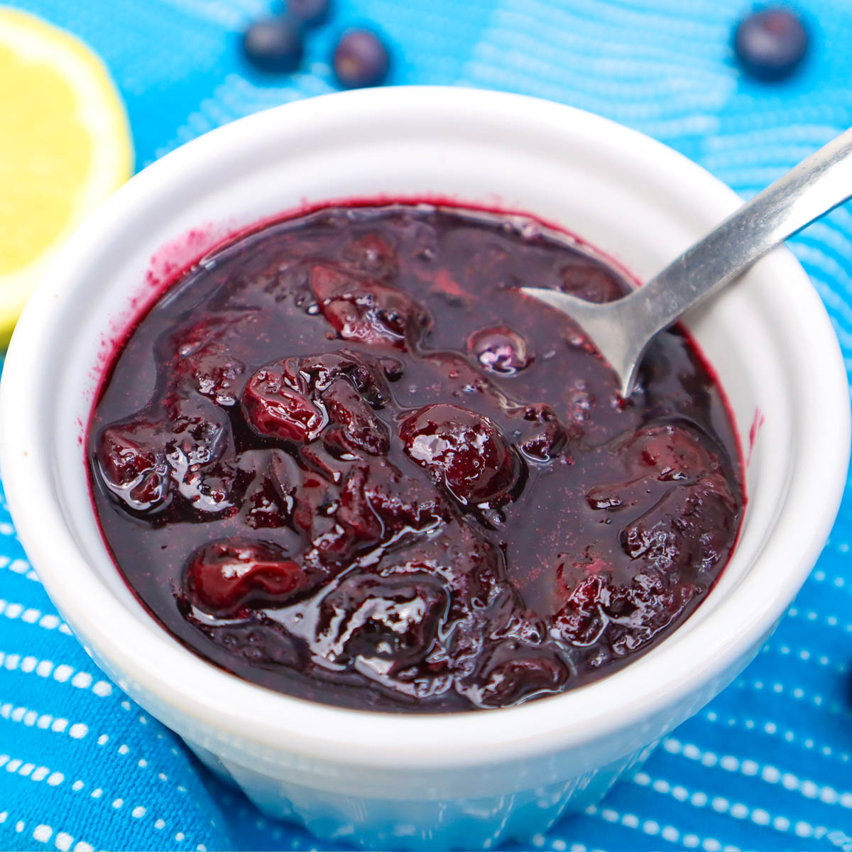 Blueberry Compote A bowl of blueberry compote with a spoon, surrounded by fresh blueberries and a slice of lemon.