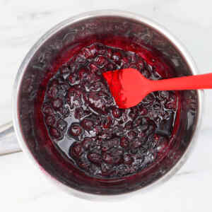 A pot of blueberry compote with a red spatula stirring it.