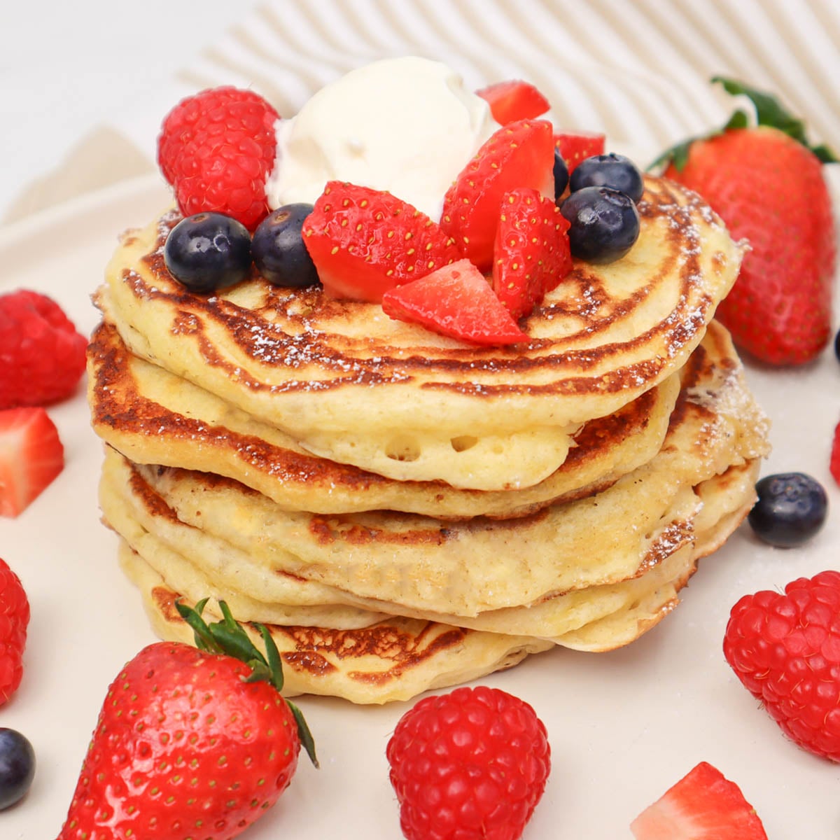 Panquecas de Leitelho Pilha de panquecas fofinhas de buttermilk cobertas com frutas vermelhas frescas e chantilly.