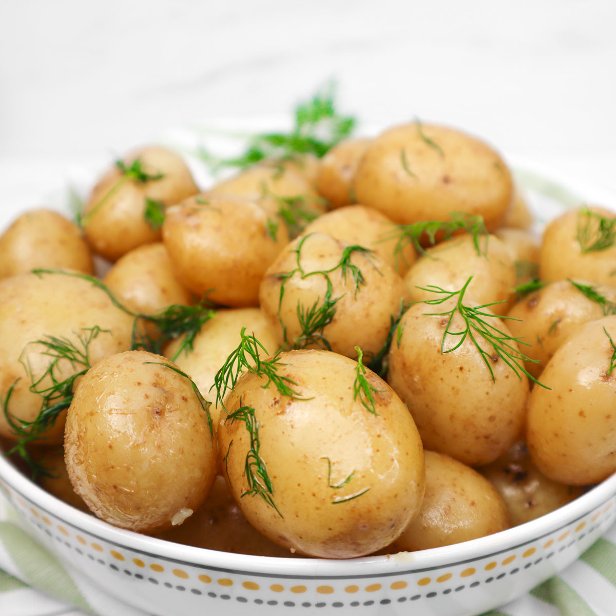 Buttery Boiled New Potatoes A bowl of buttery boiled new potatoes garnished with fresh dill.