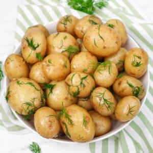 A bowl of buttery boiled new potatoes garnished with fresh dill.