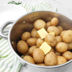 A pot filled with boiled new potatoes topped with butter.