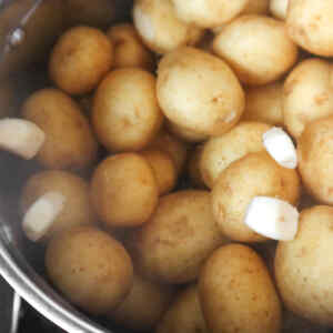 A pot filled with boiled new potatoes, with pieces of garlic floating on top.