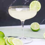 Un cocktail daiquiri guarnito con una fetta di lime, circondato da mezze fette di lime fresco su un tovagliolo verde.