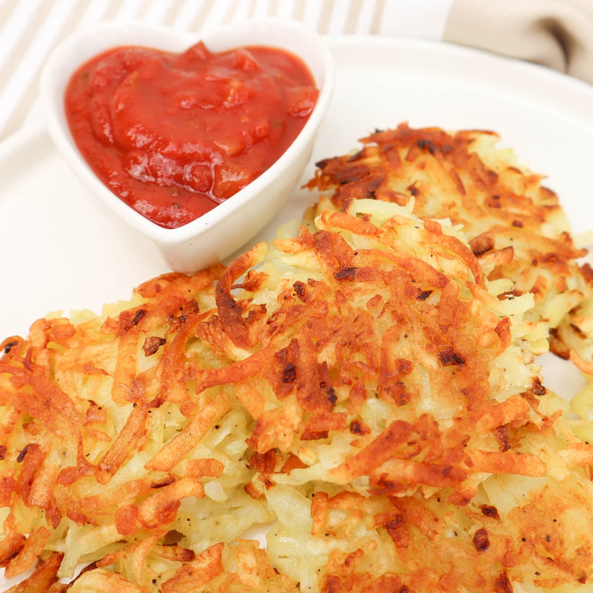 Hash Browns Crispy hash browns served with a side of ketchup sauce in a heart-shaped dish.