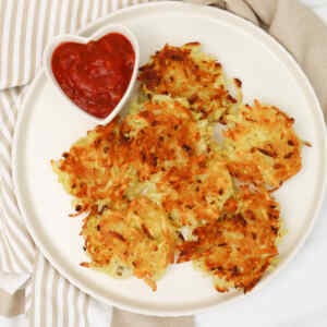 Crispy hash browns served on a plate with a heart-shaped dish of ketchup.
