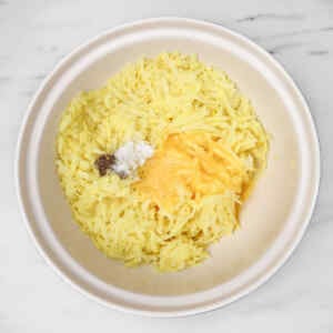 Shredded potatoes mixed with egg, salt, and pepper in a bowl.