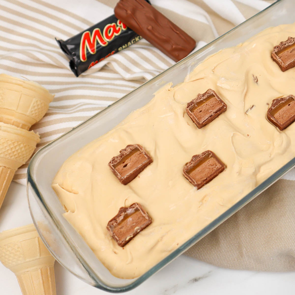 Sorvete Mars Uma taça de sorvete cremoso de caramelo coberto com pedaços de chocolate, ao lado de casquinhas de sorvete vazias.