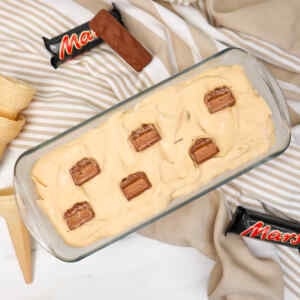 Uma taça de sorvete cremoso coberta com pedaços de chocolate, rodeada por casquinhas de sorvete e um pano listrado.