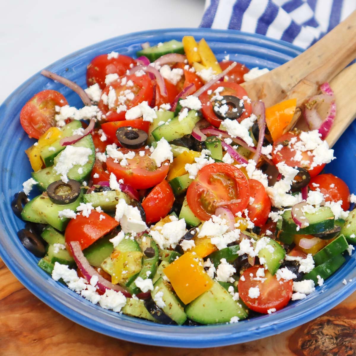 A colorful Mediterranean salad with tomatoes, cucumbers, peppers, olives, and feta cheese in a blue bowl.