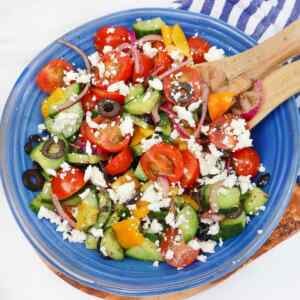 A vibrant Mediterranean salad with tomatoes, cucumbers, olives, and feta cheese in a blue bowl.