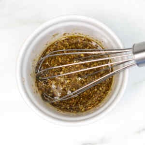 A bowl of Mediterranean salad dressing with herbs and spices mixed together.