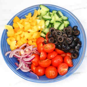 A colorful bowl of chopped vegetables including bell peppers, cucumbers, olives, red onions, and cherry tomatoes.