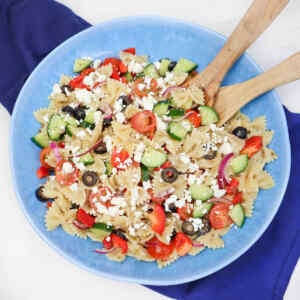 A colorful Mediterranean pasta salad with farfalle, cucumbers, tomatoes, olives, and feta cheese in a blue bowl.