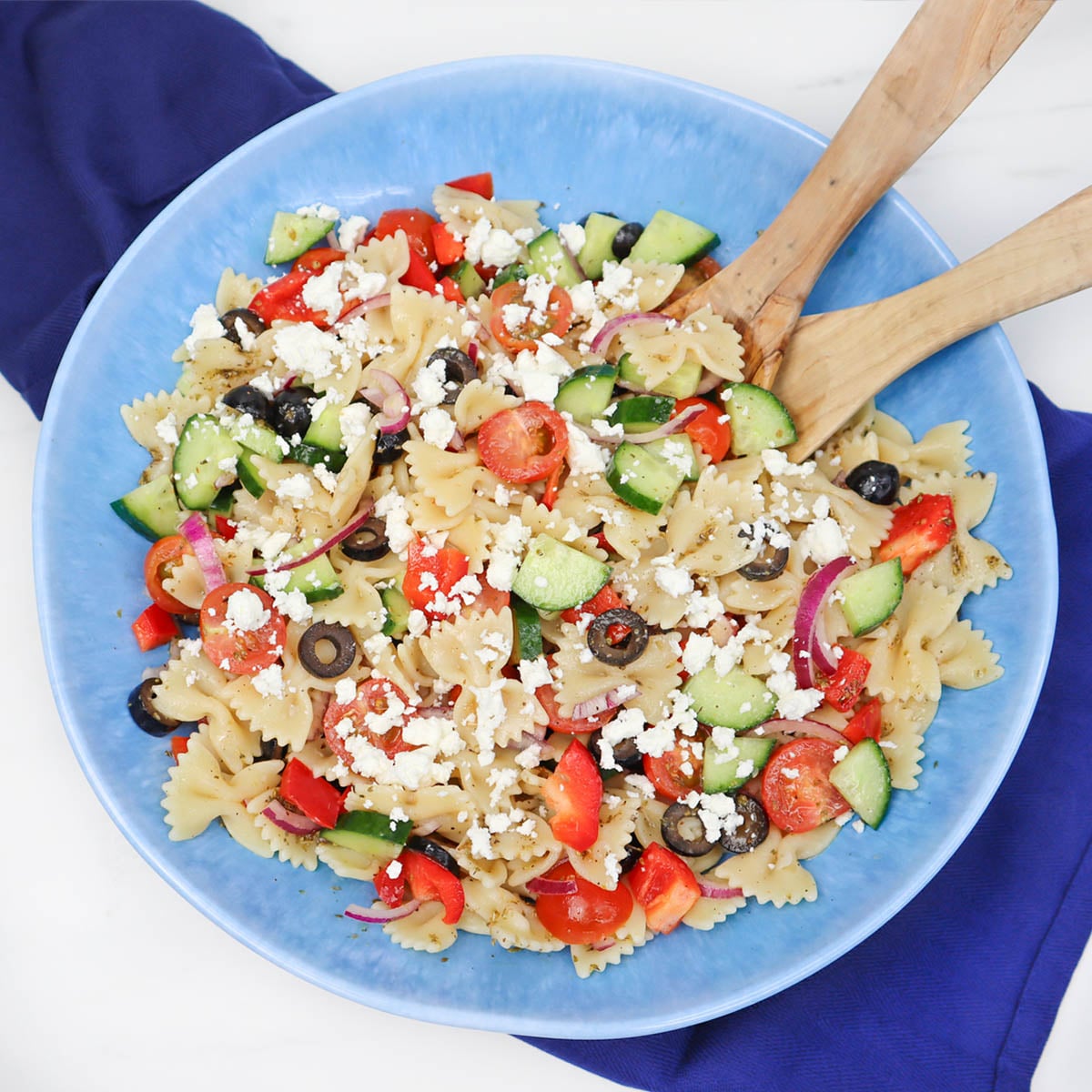 Mediterranean Pasta Salad A colorful Mediterranean pasta salad with farfalle, cucumbers, tomatoes, olives, and feta cheese in a blue bowl.