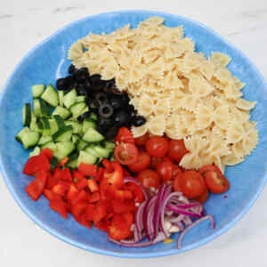 A colorful Mediterranean pasta salad with bowtie pasta, cucumbers, olives, tomatoes, sweet peppers, and red onions.