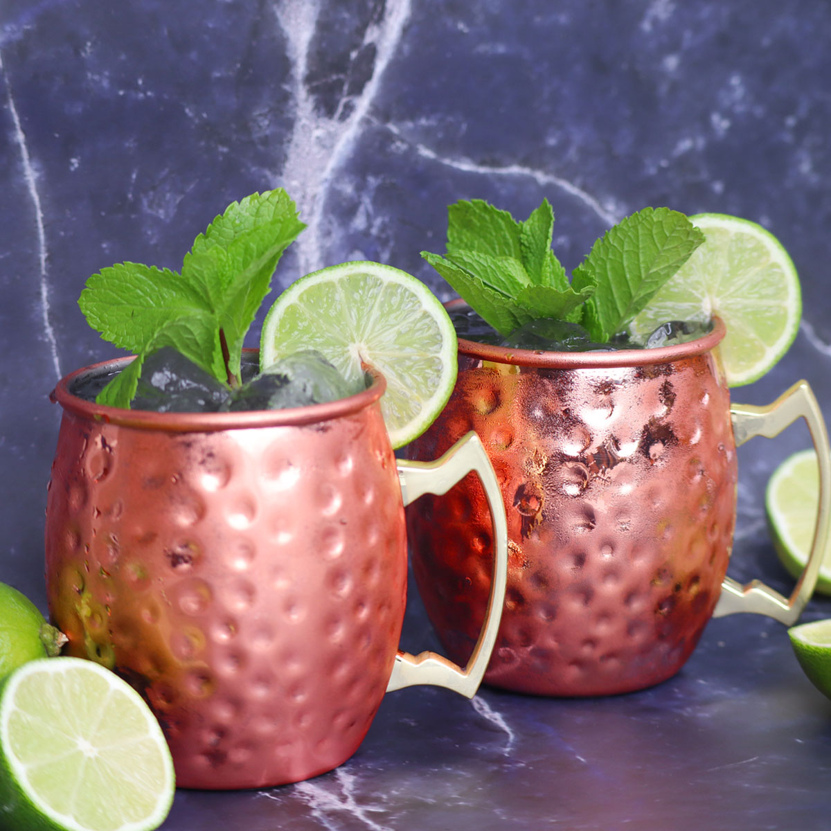 Moscow Mule Cocktail Two Moscow Mule cocktails garnished with mint and lime slices on a marble surface.
