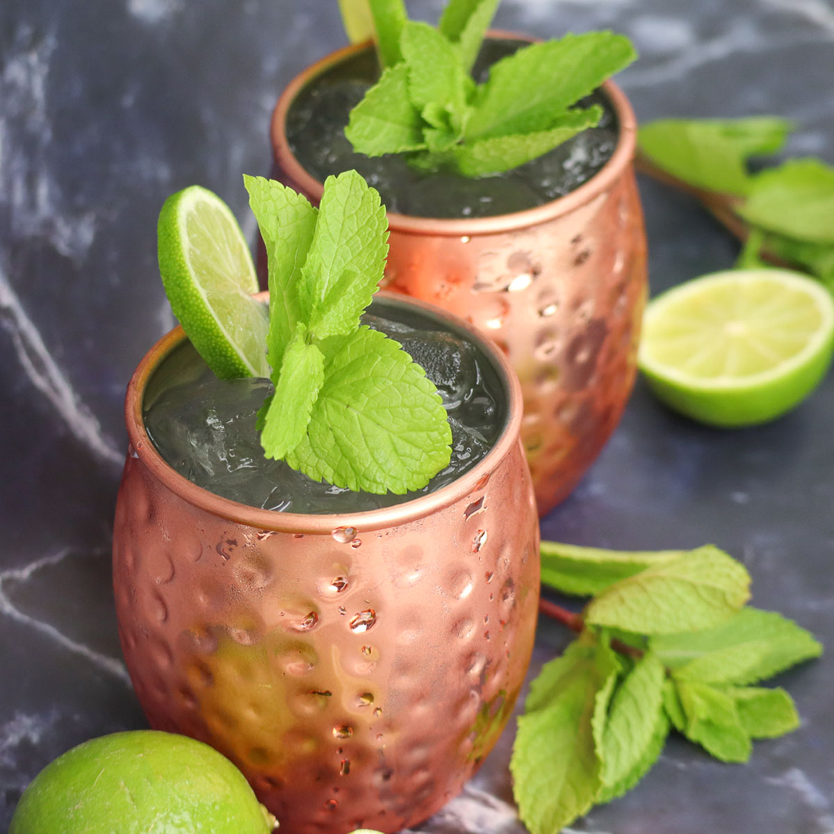 Moscow Mule Cocktail Two Moscow Mule cocktails in copper mugs garnished with mint and lime slices.