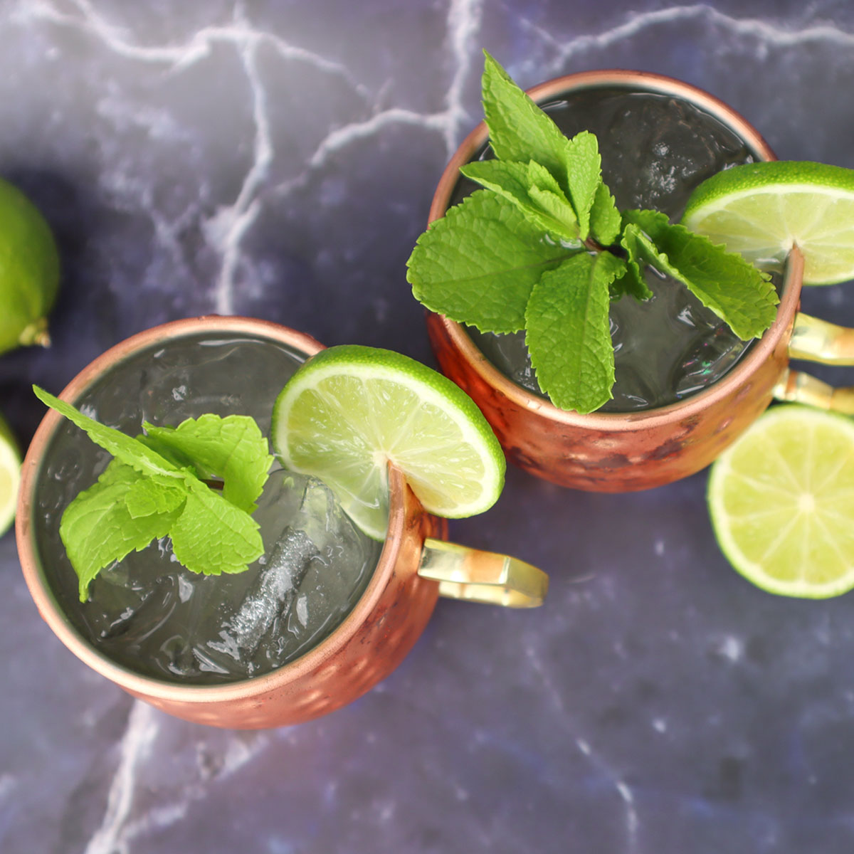 Moscow Mule Cocktail Two Moscow Mule cocktails garnished with mint and lime slices on a marble surface.