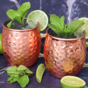 Two copper mugs filled with a Moscow Mule cocktail, garnished with mint and lime slices.