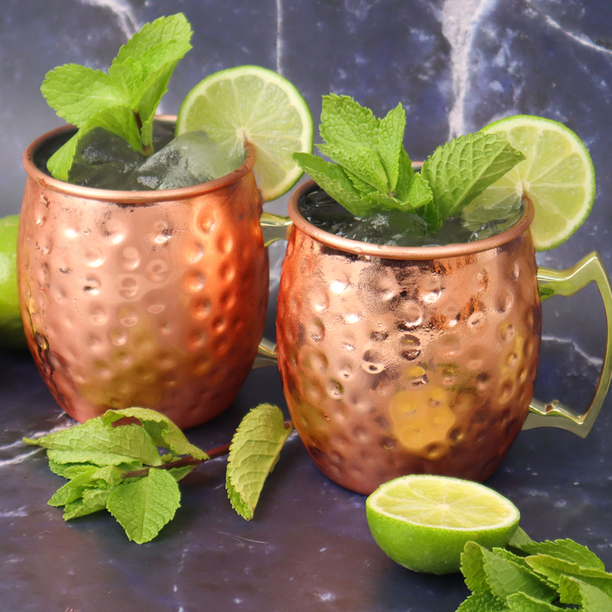 Moscow Mule Cocktail Two copper mugs filled with a Moscow Mule cocktail, garnished with mint leaves and lime slices.