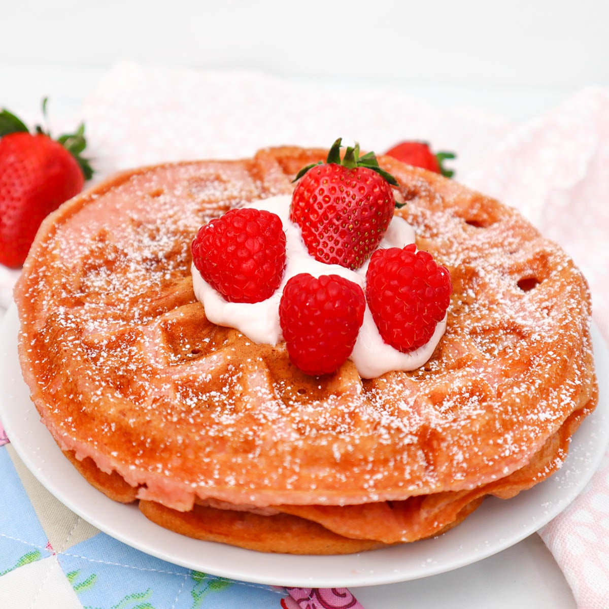 Pink Breakfast Waffles A pink waffle topped with whipped cream and fresh strawberries, dusted with powdered sugar.