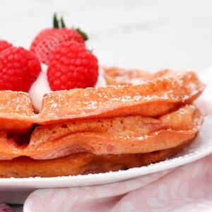 Fluffy pink waffles topped with raspberries and whipped cream, dusted with powdered sugar.