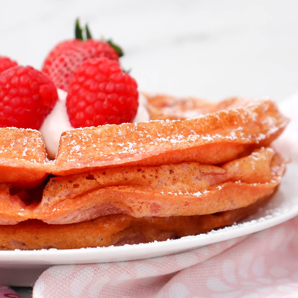 Pink Breakfast Waffles Fluffy pink waffles topped with raspberries and whipped cream, dusted with powdered sugar.