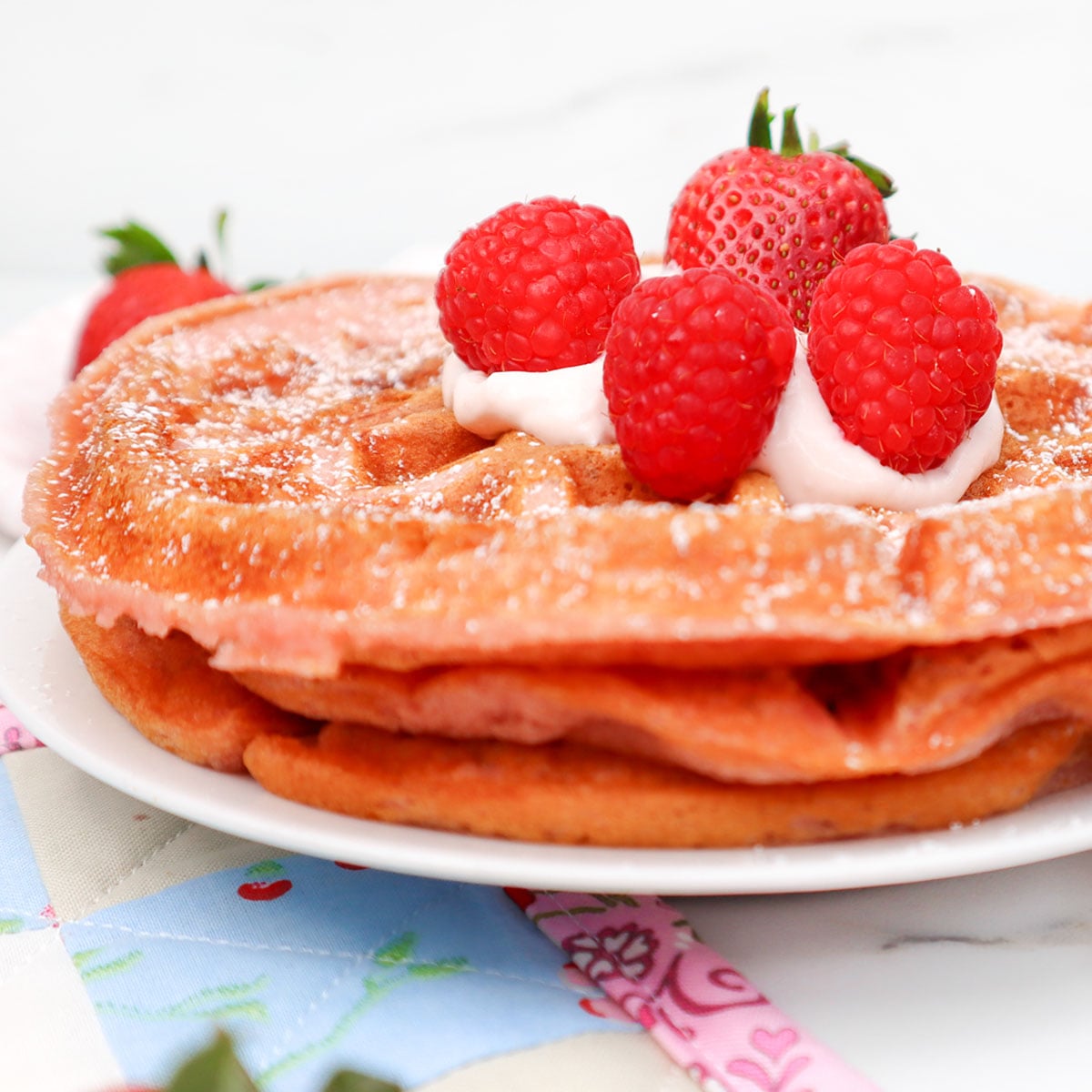 Pink Breakfast Waffles Fluffy pink waffles topped with raspberries and whipped cream on a plate.