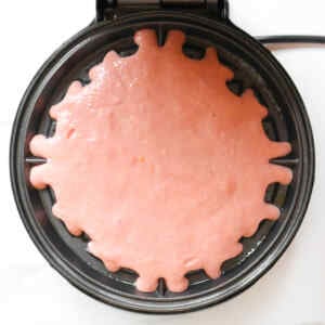 Pink waffle batter in a waffle maker, ready to cook.