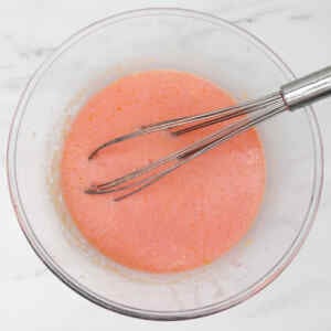 A bowl of pink waffle batter with a whisk resting inside.