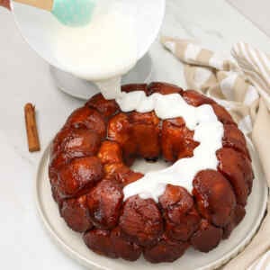 Creamy glaze is being poured over a freshly baked pull-apart monkey bread.