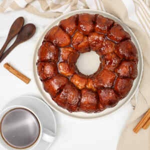 A round pull-apart monkey bread on a plate, accompanied by a cup of coffee and cinnamon sticks.