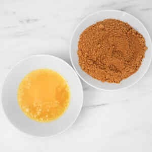 Melted butter in a bowl next to a bowl of brown sugar on a marble surface.