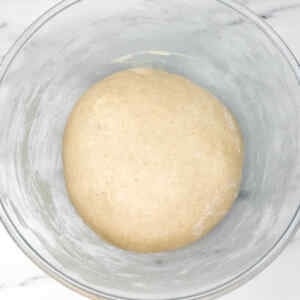 A smooth ball of dough resting in a glass bowl.