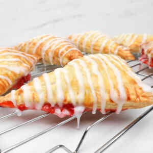 Kue pai stroberi berwarna cokelat keemasan yang disiram dengan lapisan gula di atas rak pendingin.