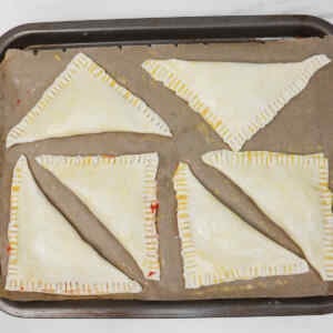 Kue pai stroberi yang belum dipanggang disusun di atas loyang yang dilapisi kertas roti.