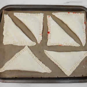 Kue pai stroberi yang belum dipanggang disusun di atas loyang yang dilapisi kertas roti.